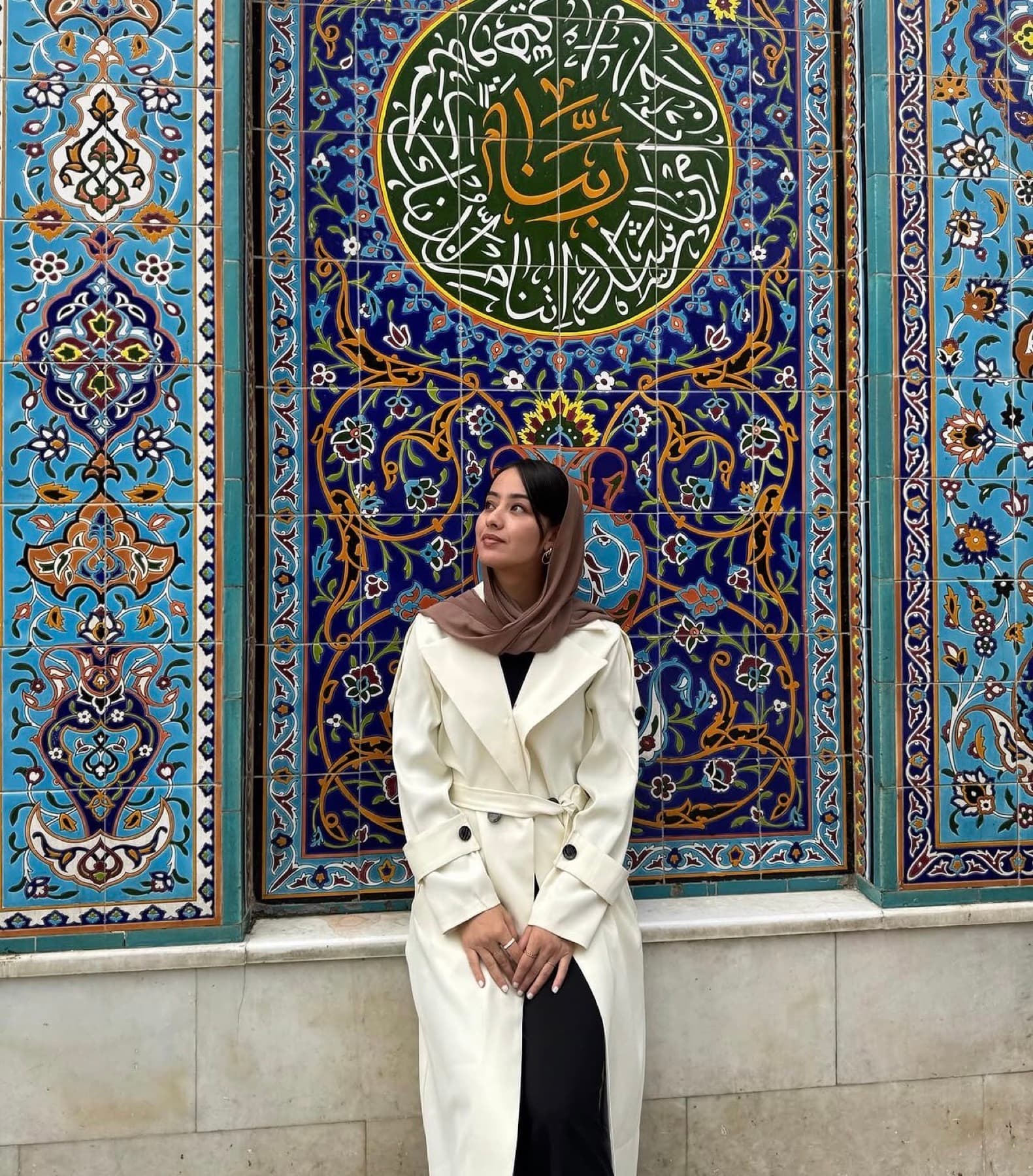 The founder of Rangin Poshak Boutique standing in front of colourful Afghan cultural tilework.
