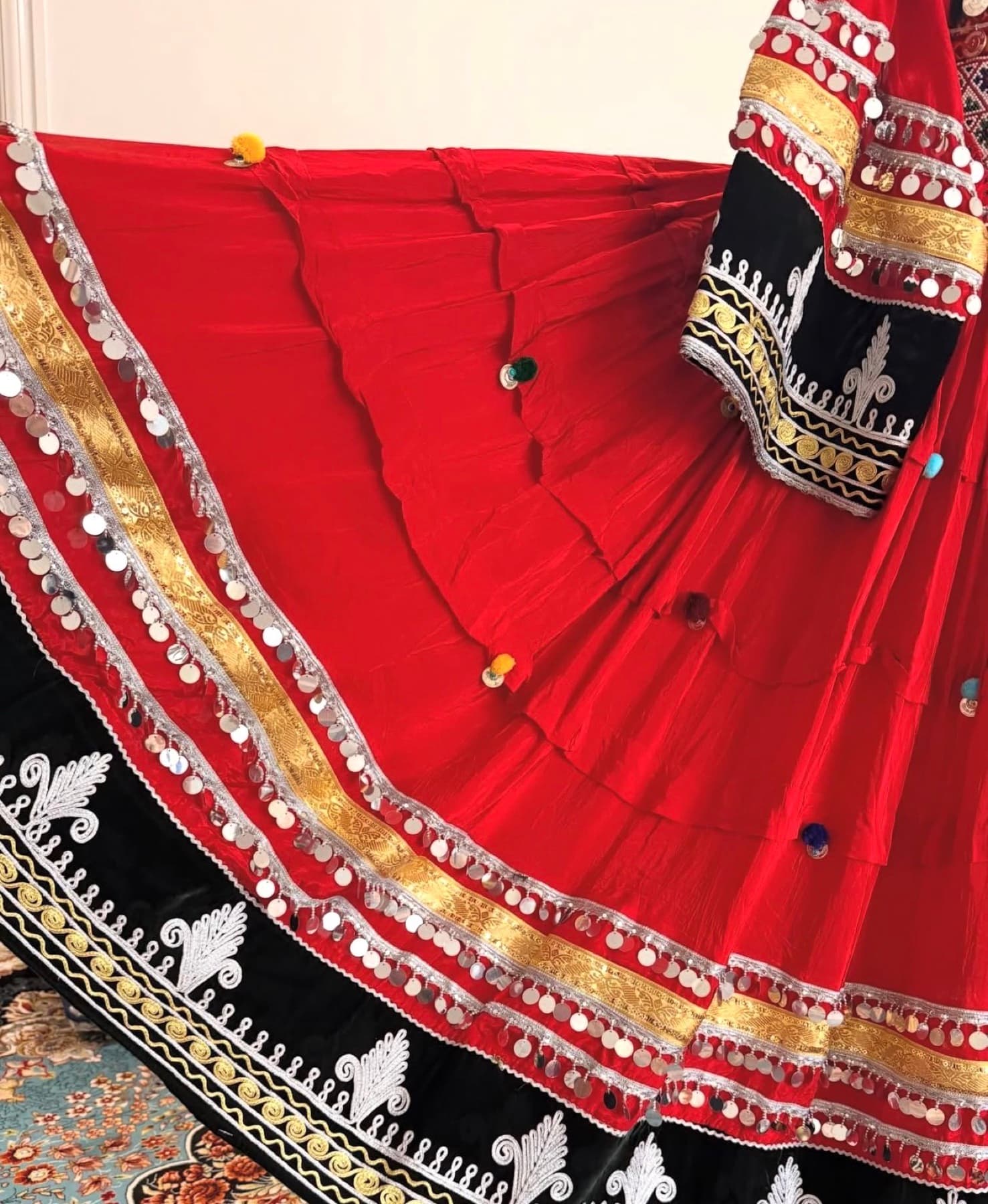 Close detail of an Afghan dress with gold coinwork and rich red embroidery.