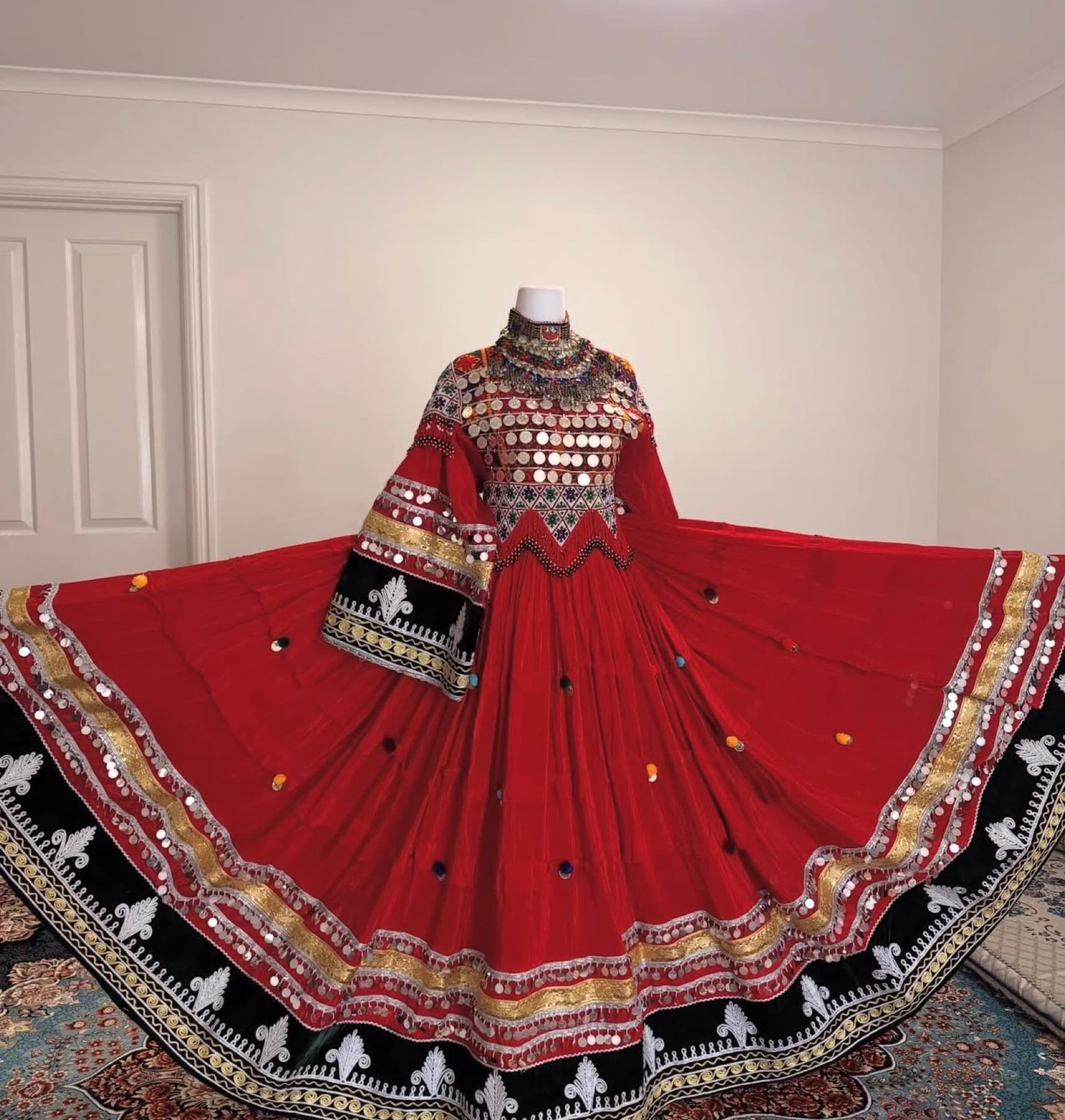 Wide display of a red Afghan traditional dress with gold trim, coinwork, and black velvet borders.